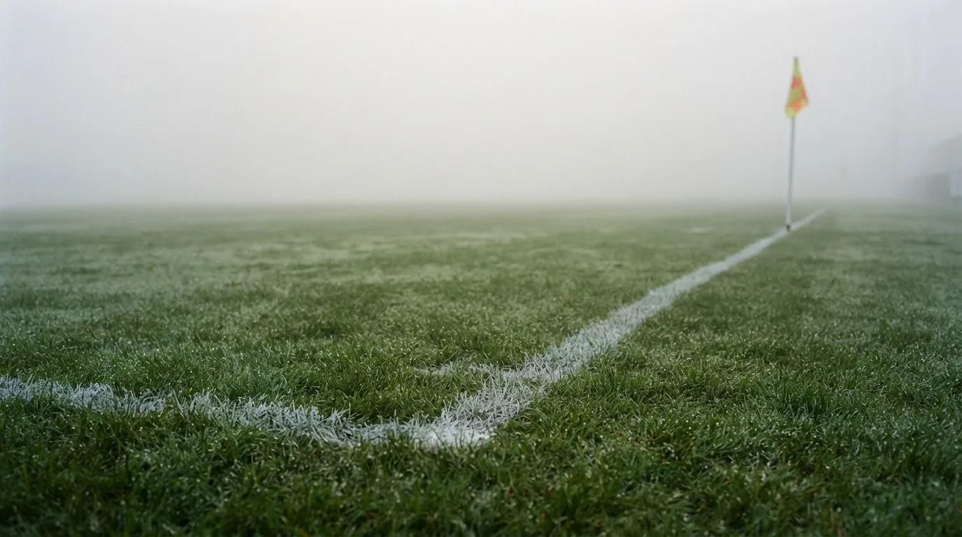 Der Rand eines Spielfelds mit weißer Linie und Eckfahne bei Nebel am frühen Morgen, ohne Menschen.