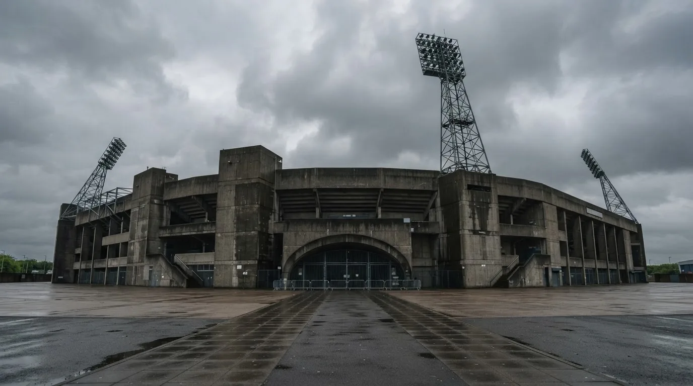 Ein leeres Stadion von außen, hohe Flutlichtmasten vor einem grauen Himmel mit Regenwolken.