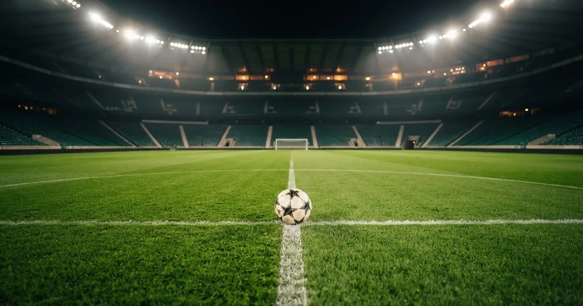 Ein Fußball liegt auf dem Rasen eines leeren Stadions bei Flutlicht, im Hintergrund unscharfe Tribünen ohne erkennbare Beschriftung.