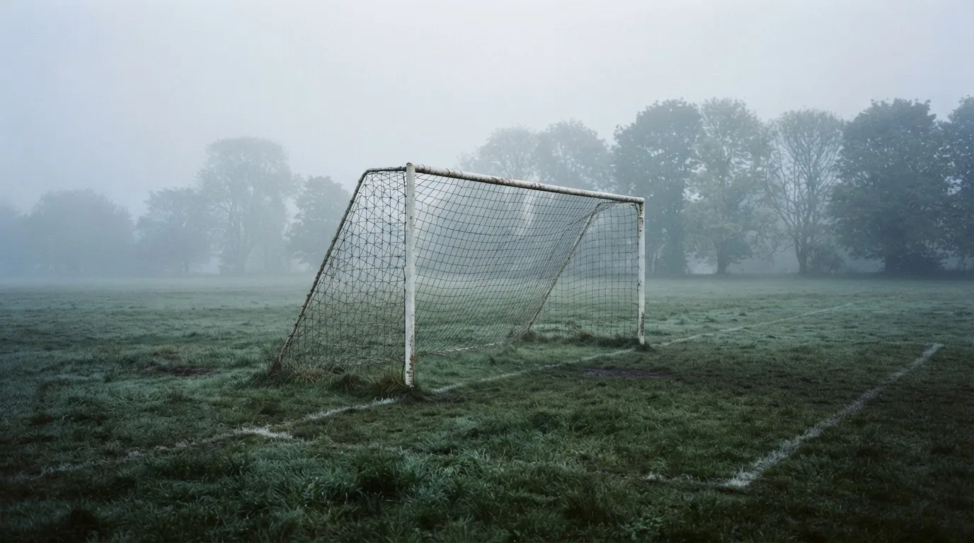 Ein Fußballtor mit Netz im Morgennebel auf einem leeren Platz, die Linien nur schwach zu erkennen.