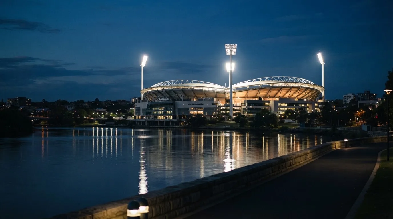 Ein Stadion unter Flutlicht aus der Ferne gesehen, im Vordergrund ein ruhiger Fluss und ein Fußweg.
