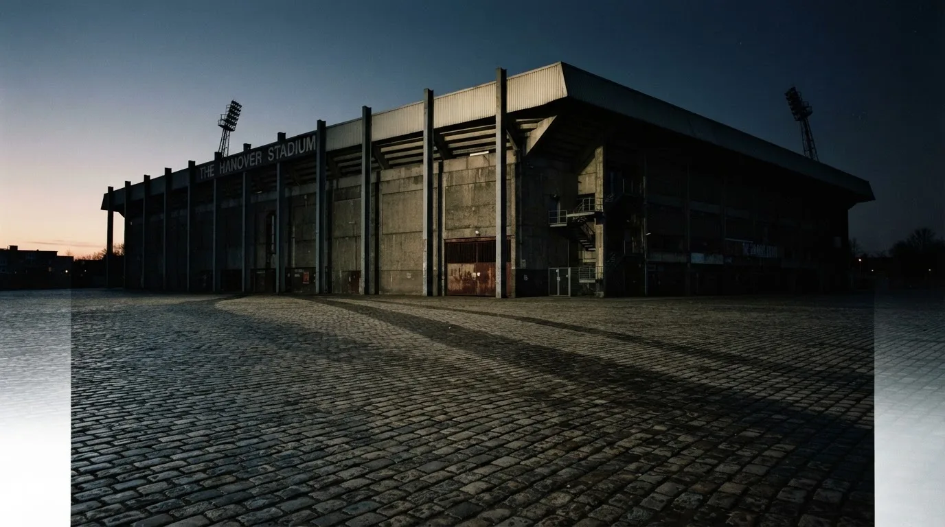 Die Rückseite einer Tribüne bei Dämmerung, davor ein menschenleerer Vorplatz mit Pflastersteinen.