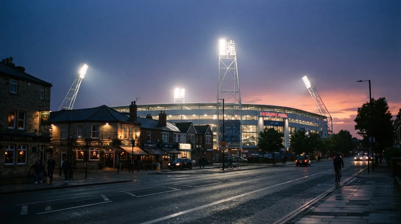 Ein Stadion aus der Ferne bei Flutlicht, davor eine ruhige Straße in der Abenddämmerung.