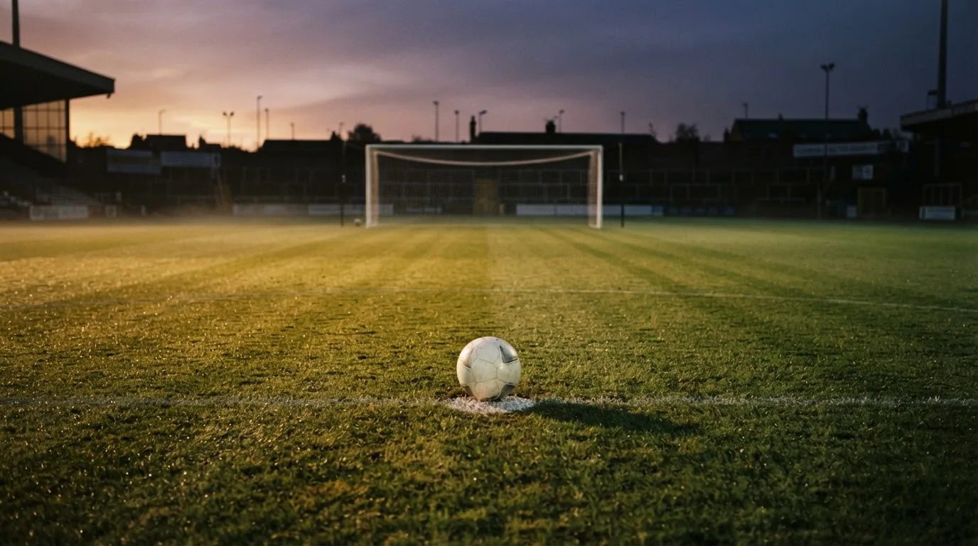 Ein Fußball liegt auf dem Elfmeterpunkt eines leeren Platzes im Abendlicht.