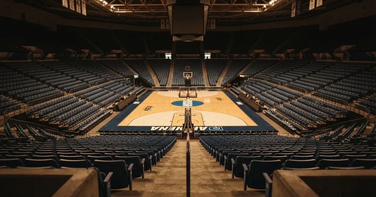 Eine leere Basketballhalle von einer oberen Tribünenreihe aus gesehen, Parkett und Körbe im Licht der Hallenstrahler.