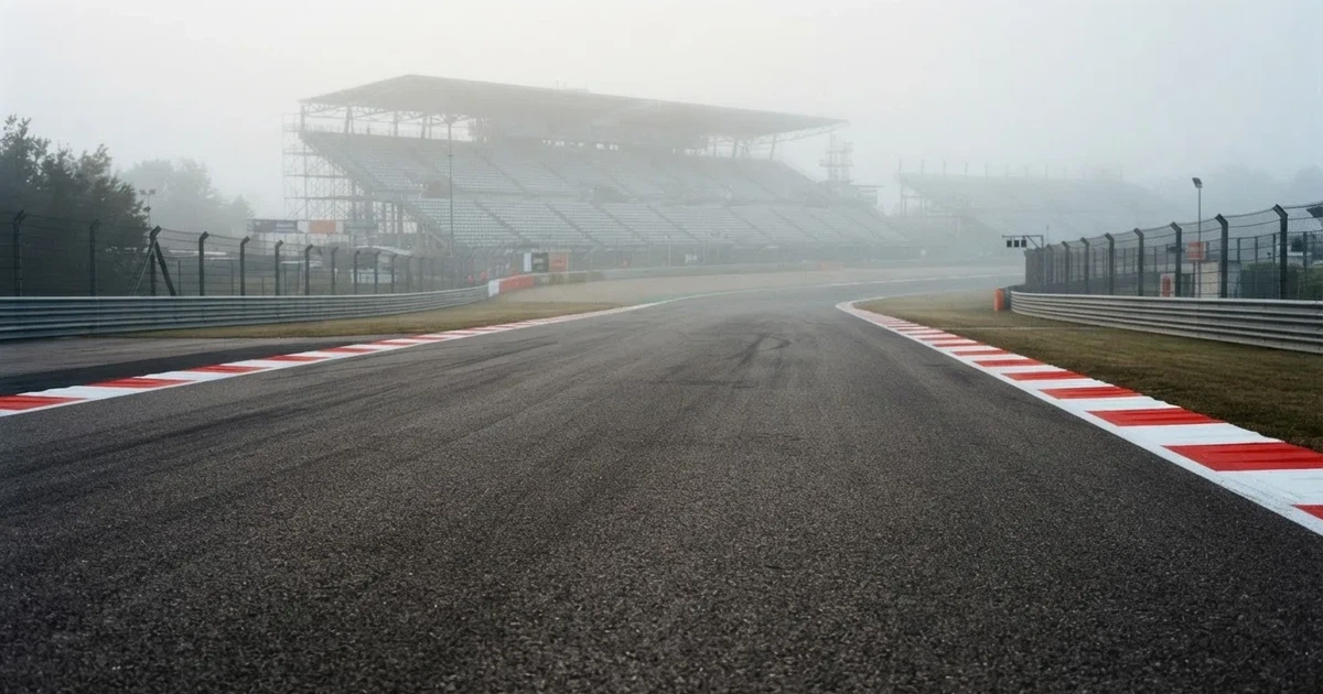Eine leere Rennstrecke im Morgennebel, Asphalt mit rot-weißen Randsteinen, im Hintergrund Tribünen in der Ferne.