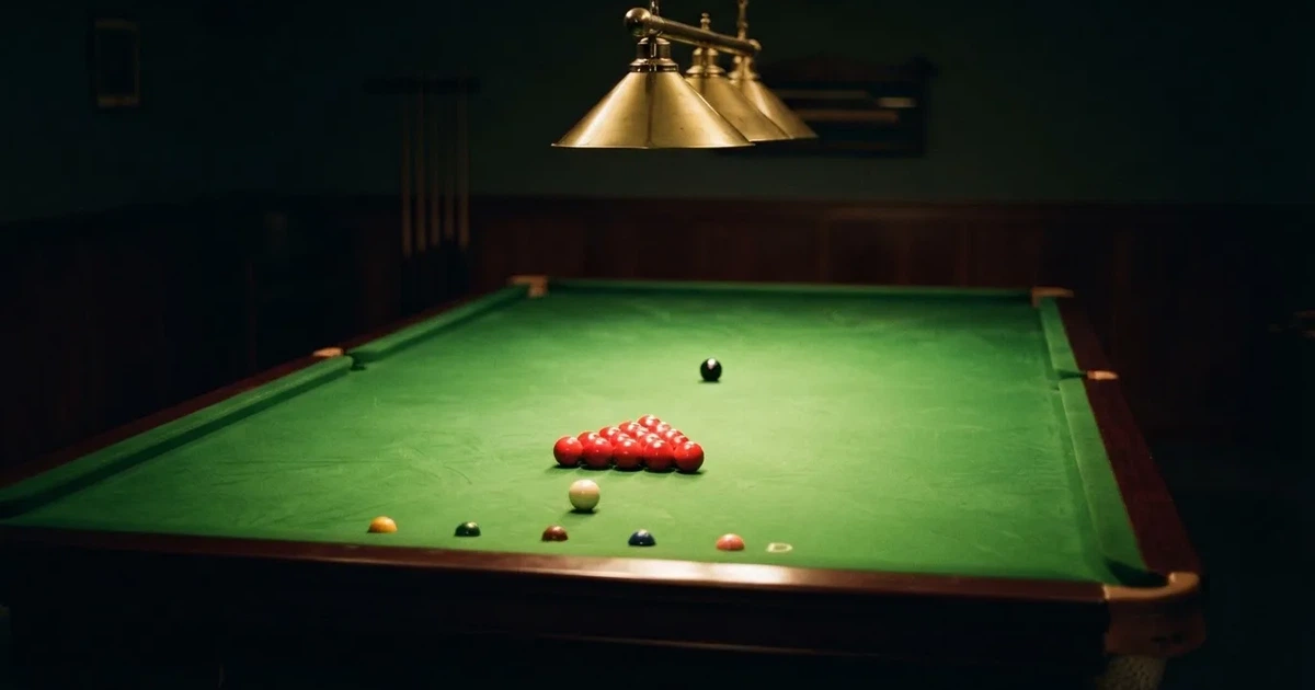 Ein Snookertisch mit grünem Tuch und aufgebauten roten Kugeln in einem abgedunkelten Raum unter einer hängenden Lampe.